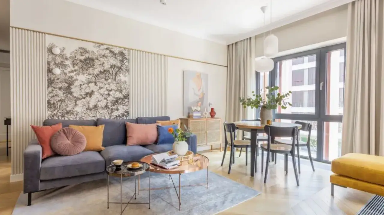 Stylowy salon z szarą kanapą, kolorowymi poduszkami i tapetą z drzewami. Inspiracja, jak powiesić 4 obrazy na ścianie, by stworzyć harmonijną kompozycję.