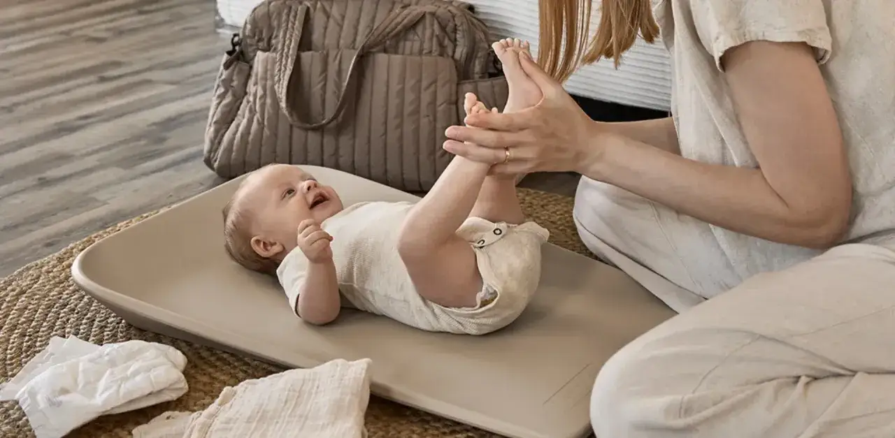 Mama przewija dziecko na przewijaku. Zastanawiasz się, jaki przewijak wybrać? Ten jest wygodny i bezpieczny.