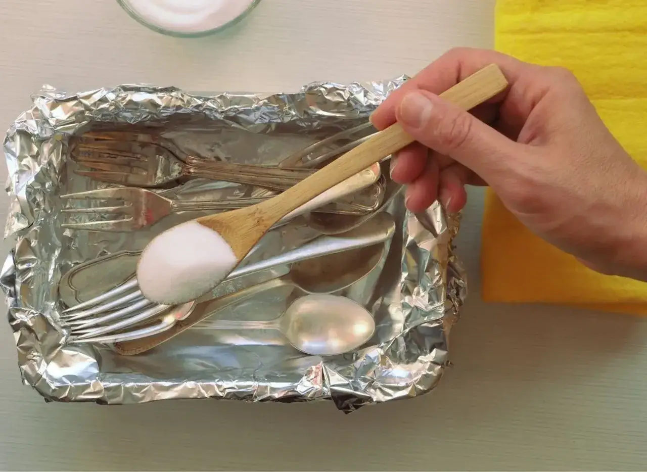 Łyżka z sodą do czyszczenia sztućców w folii aluminiowej. Domowy sposób na przywrócenie blasku metalowym przedmiotom.