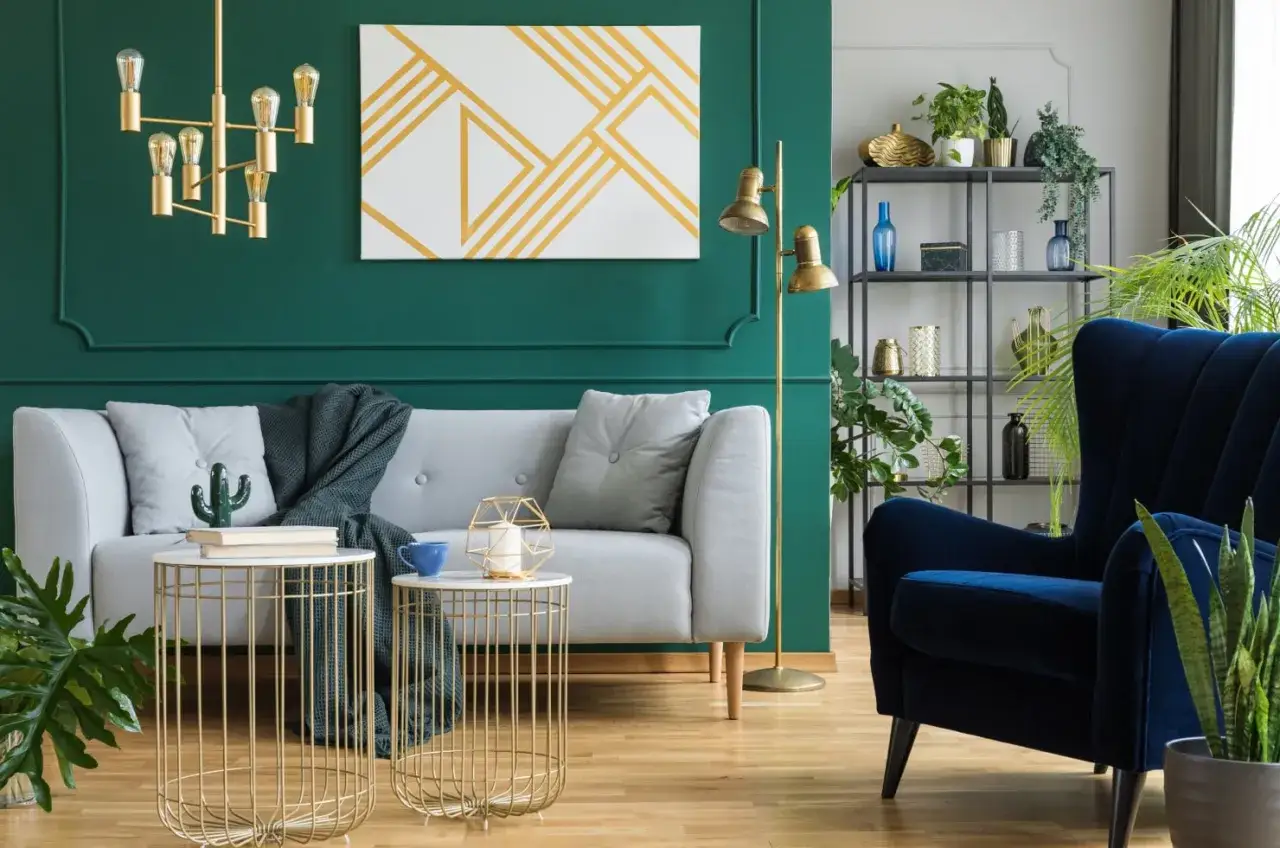 Eleganckie wnętrza art deco: szara kanapa, granatowy fotel, złote stoliki i zielone ściany tworzą stylową przestrzeń.