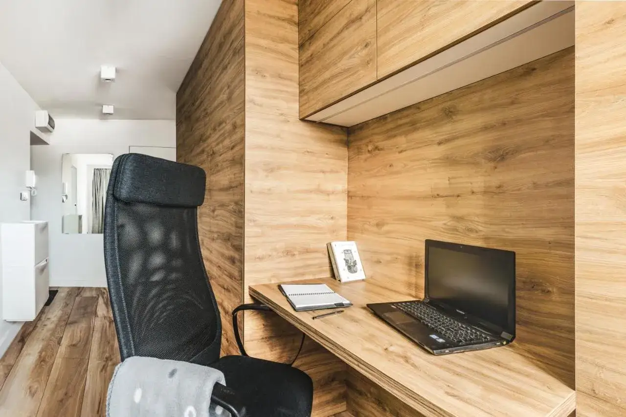 Mały pokój inspiracje: przytulne biurko z laptopem i notesem, obok ergonomiczne krzesło. Drewniane wykończenie ścian tworzy ciepłą atmosferę.