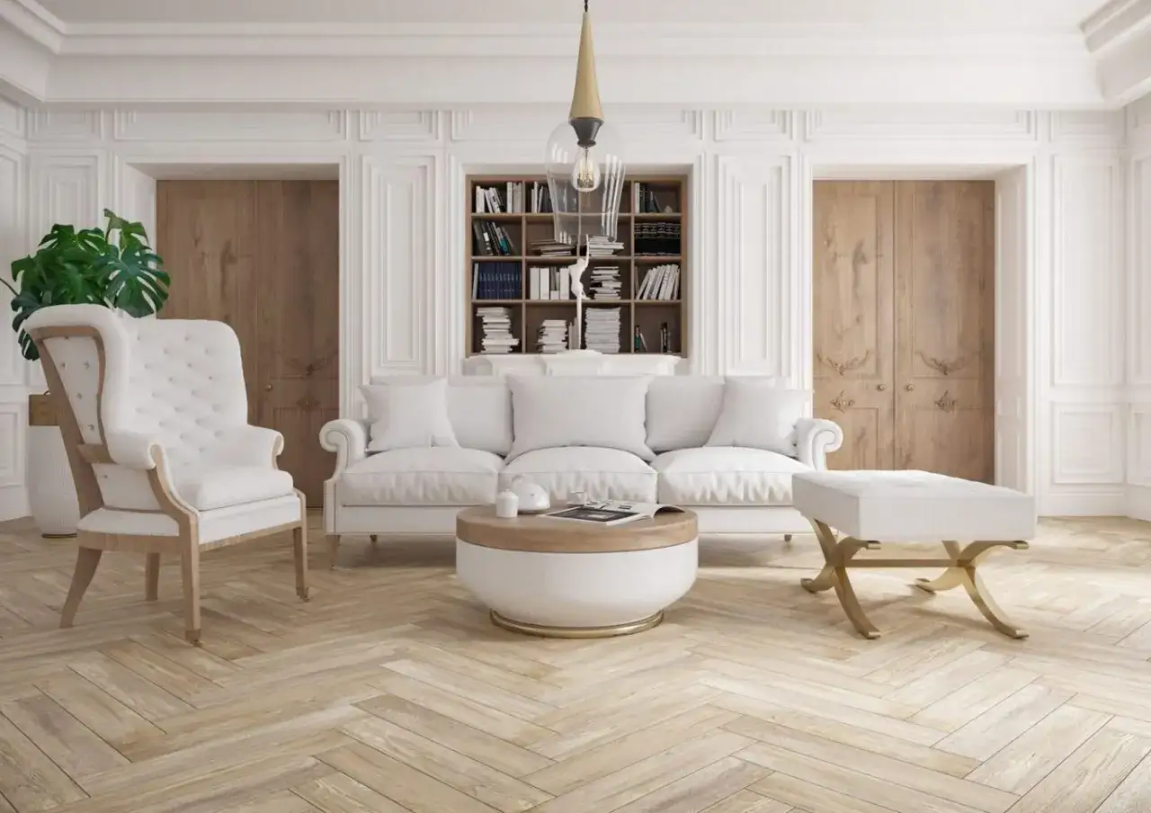 Elegancki salon z białą sofą, fotelem i pufą. W tle regał z książkami i drewniane drzwi. Nowoczesna sztukateria ścienna dodaje wnętrzu klasy.