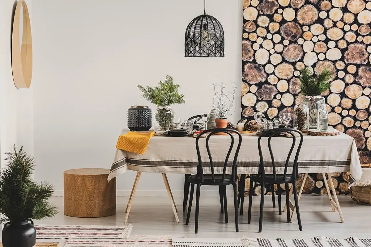 Ściana z drewna w jadalni to świetny pomysł na stworzenie przytulnej atmosfery. Stół nakryty lnianym obrusem, czarne krzesła i dekoracje z szyszek dopełniają rustykalny styl.