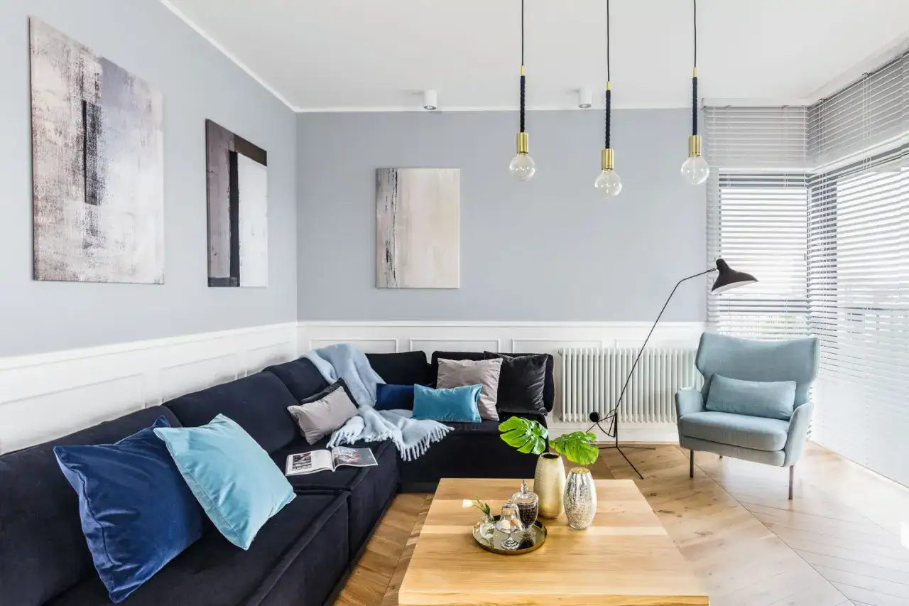 Nowoczesny salon z granatową kanapą i błękitnymi poduszkami. Inspiracje kolorystyczne: szarości, błękity i granaty tworzą spokojną atmosferę.