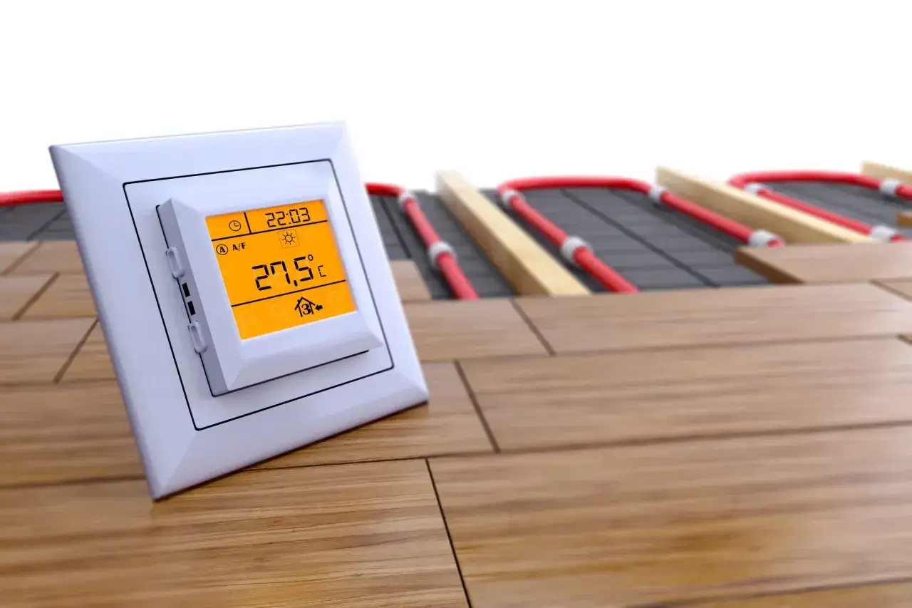 Termostat pokazuje 27,5°C. Widoczne są czerwone rurki systemu ogrzewania podłogowego pod drewnianą podłogą. Idealne panele na ogrzewanie podłogowe zapewnią komfort.